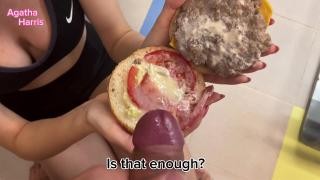A blonde in glasses gives her friend a blowjob while holding a burger.